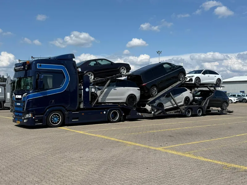 Beladen blauwe Scania-autotransporter onder een blauwe lucht